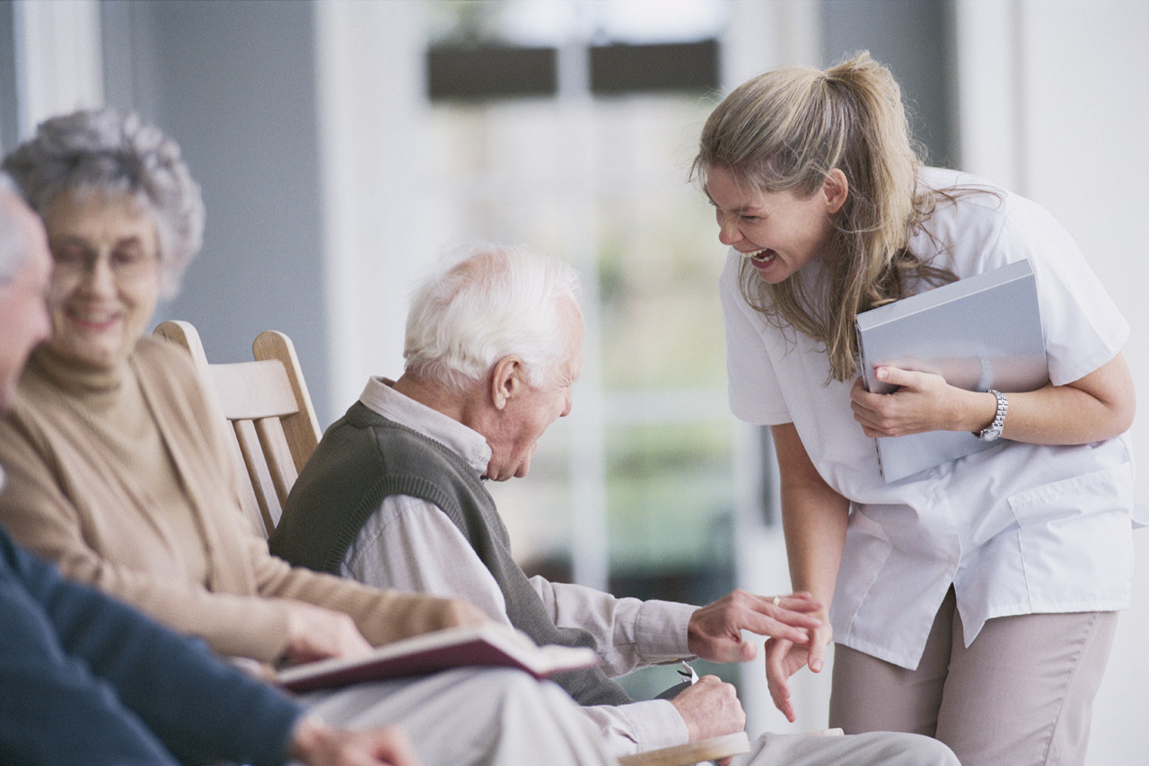Nurse laughing and talking with an elderly man sitting beside other seniors.
